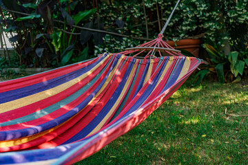  A vibrant, multi-colored striped hammock hangs invitingly in a lush green garden, promising...