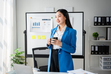 A woman in a blue jacket is holding a cup of coffee in front of a white board wi