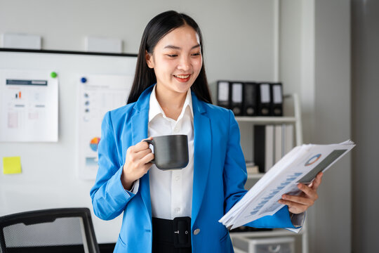 A woman in a blue jacket is holding a mug and reading a paper