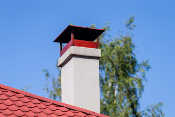 modern house white chimney with red cap on red tiled roof under blue sky and green trees residential heating ventilation pipe outdoor architectural detail exterior flue system sunny day scene