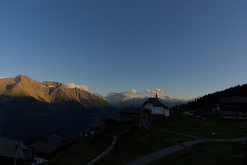 A serene church with a cross-topped steeple stands silhouetted against snow-capped mountains and a...