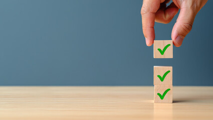 Hand Placing a Checkmark Block on a Stack Representing Approval, Validation, and Positive Results on a Wooden Table Against a Neutral Background