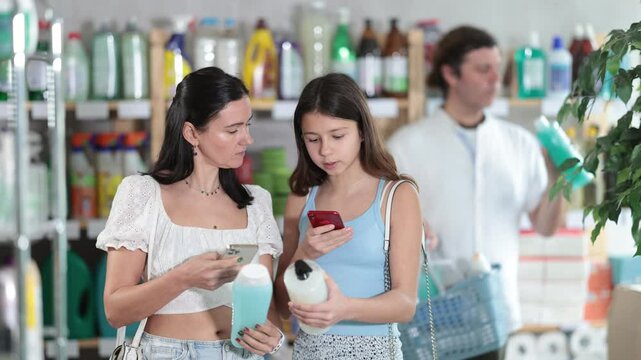 Positive mom and daughter scanning barcode on shampoo while, man choosing something behind in summer. High quality 4k footage