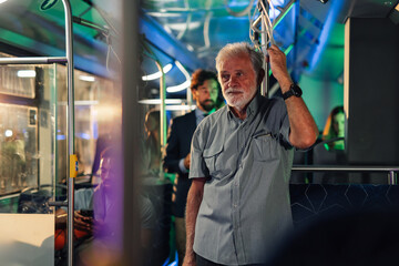 Senior man holding handrail while riding public transport at night