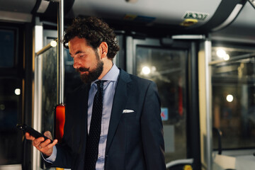 Elegant businessman using smartphone on public transport at night