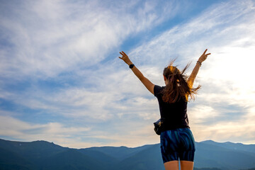 Woman celebrating freedom on mountain summit. A young woman stands on a mountain peak with arms...