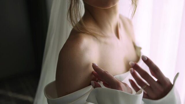 Beautiful unrecognizable bride in wedding dress with delicate skin enjoys moment in anticipation of happy moment of meeting her beloved groom. Woman strokes her collarbone flirting with her husband