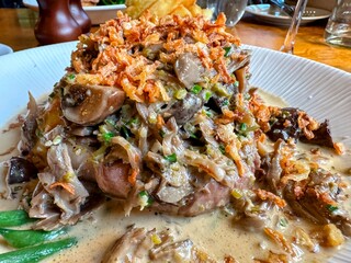 Pork cheeks garnished with crispy onions on plate in restaurant
