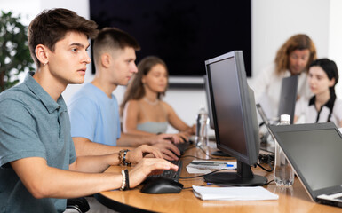 Obraz premium Concentrated interested junior software developer working in IT startup, sitting at computer desk and coding with group of coworkers..