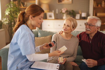 Obraz premium In a bright living room, a female nurse is explaining prescription medications to an elderly couple. The nurse is holding a pill bottle and packs of pills, pointing to them.