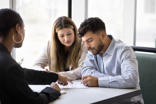 Sign here. Satisfied clients biracial family husband wife signing paper contract agreement on meeting with trusted saleswoman realtor insurer buying selling home property taking loan making investment