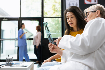 General practitioner analyzing X ray test results with asian woman in a lobby, providing guidance...
