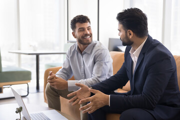 Casual business discussion. Smiling young businessman talk to male colleague sitting on couch...