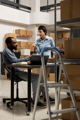 Diverse team at desk discussing order processing to guarantee distribution in a tightly packed storage room filled with products and boxes. Organized structure of a small scale business.