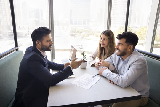 Stress free deal making. Positive male insurance agent real estate specialist win over multiethnic family couple of clients give professional advice in casual relaxed setting fostering trust comfort - Powered by Adobe