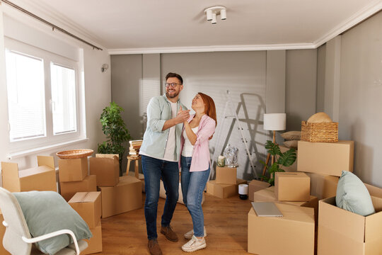 A couple joyfully engages with each other, surrounded by cardboard boxes in their new living room. They appear happy and excited about this new chapter in their lives. - Powered by Adobe