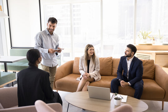 Business training in relaxed setting. Multiracial employees group international company department staff gather in cozy coworking area for coaching session engaged in friendly collaborative discussion