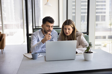 Thinking by laptop. Multiethnic colleagues business partners mid aged woman mentor young man intern...