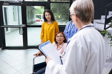 Wheelchair user discussing with medic at routine checkup at the clinic, offering guidance and...