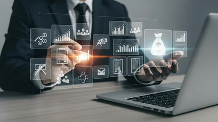Businessman interacting with digital financial icons near laptop on a desk in a dark suit - Powered by Adobe