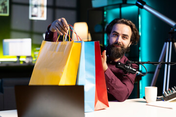 Media star holding colorful shopping bags in hand, showing fans purchases he recently got, filming...