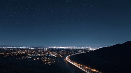 City lights glow below dark sky with road leading to it.