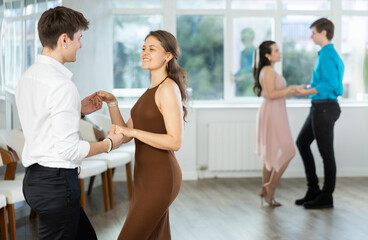 Fototapeta premium While doing rehearsal of reporting concert, guy and girl participants of dance workshop perform quickstep. Two couples practice their skills in performing quickstep during attending dancing school.