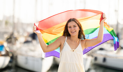 Young woman in summer dress with LGBT flag on sea port with yachts