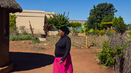 Africa village chores, single elderly african woman walking in the yard, round traditional house...