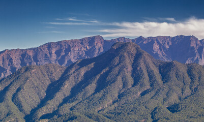 Photograph of the Caldera de Taburiente in the foreground with its pine forests and rock walls inside the caldera on a clear day.