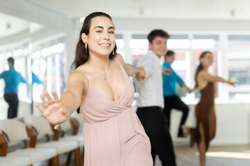 Smiling enthusiastic young dark-haired girl rehearsing upbeat jive dance moves with male partner in...