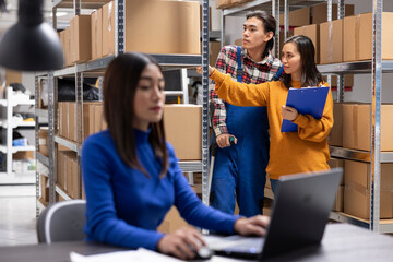 Asian employee using crutches to walk in storage room and manage orders for distribution. Small...