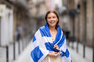 Young woman in summer dress wrapped in Greek flag on city street