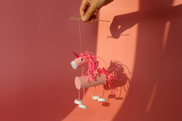 a whimsical handmade unicorn marionette puppet held by a hand. crafted from toilet paper roll...