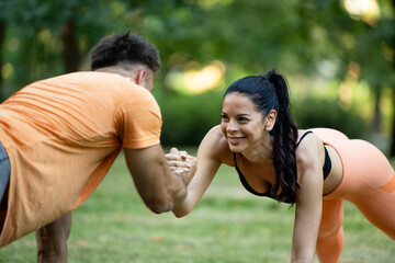 Fitness woman doing plank exercise with her personal trainer outdoors in the park.