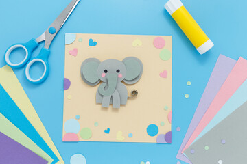Top-down view of colorful workspace with gray paper elephant and crafting materials. Ideal for brands in children education, craft kits, or artistic content creators promoting playful projects.