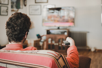 Man changing channels on his television using the remote control while sitting on the couch.
