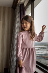 Lifestyle portrait of happy smiling little girl standing near the window in hotel room
