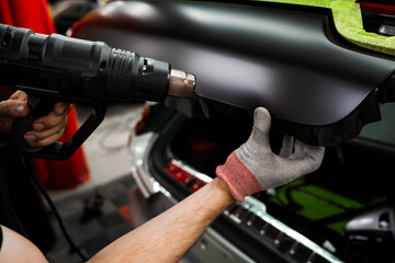 Car Vinyl Wrapping with Heat Gun. Applying black vinyl wrap to car with heat gun ensures precise...