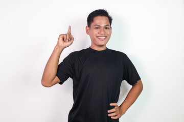 Smiling young Asian man wearing black clothing confidently points upward, symbolizing positivity...