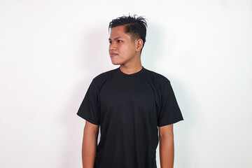 Portrait of Asian man wearing a black t-shirt while standing against a white background and gazing...