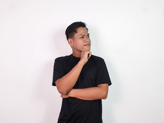 A young Asian man stands thoughtfully with his hand on his chin, wearing a black shirt against a...
