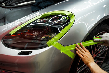 Car Surface Masking for Matte Black Vinyl Wrap Preparation. Technician applies masking tape around...