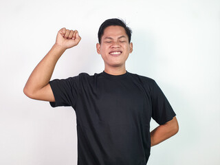 A young Asian man in a black shirt enthusiastically gestures, signifying joy, success, or victory....