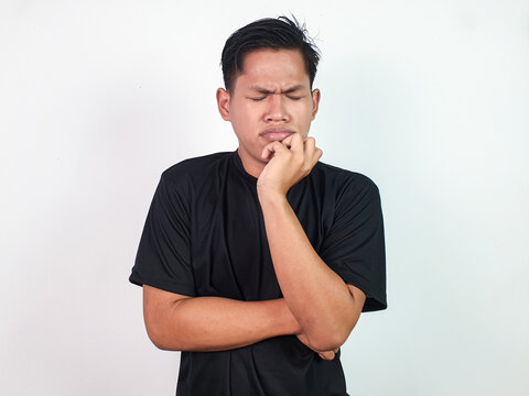 A young Asian man wearing a black shirt is posing thoughtfully, with one hand on his chin and a contemplative expression, standing against a white background.