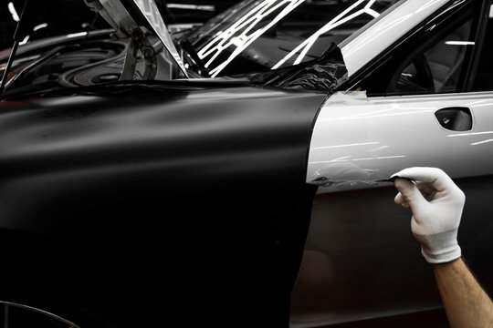 Full Panel Car Vinyl Wrapping. Large-scale vinyl wrap installation transforms the vehicle exterior with matte black film. Car wrap application changes vehicle appearance.