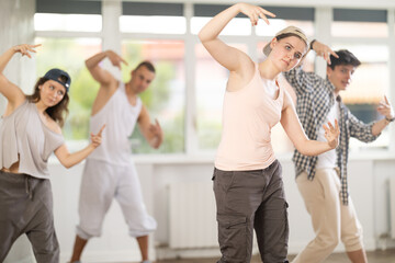 Positive young lady engaged in hip-hop together with other attendees of dancing courses for...