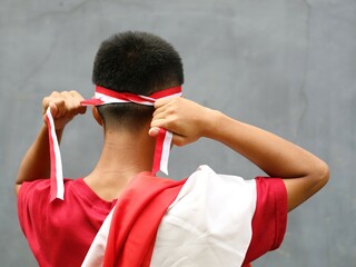 man in red shirt with Indonesian flag on his shoulder, his hand holding ribbon on his head, back...