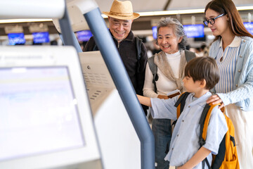 Asian family using airport self check-in kiosk together, multigenerational group interacting with...