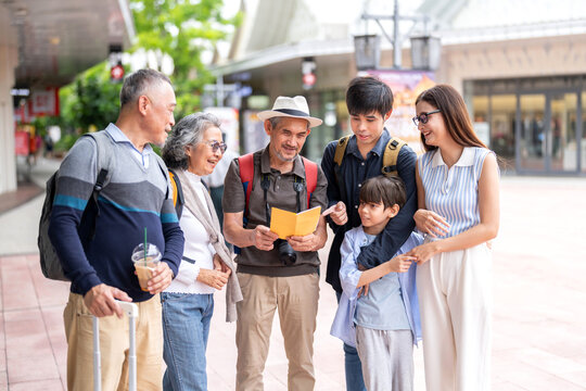 Family multigenerational travelers reading tourist guide and map planning travel with grandparents parents and child, smiling group enjoying vacation moment, big family trip, lifestyle and tourism